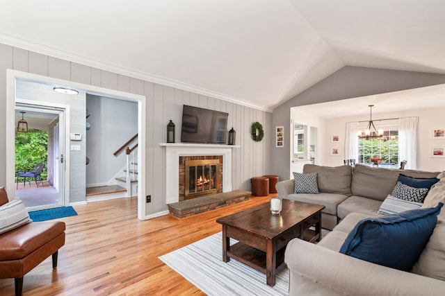 living area featuring stairs, a chandelier, light wood-type flooring, lofted ceiling, and a fireplace