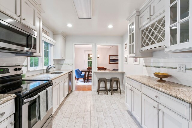 kitchen featuring stainless steel appliances, a sink, decorative backsplash, light wood finished floors, and glass insert cabinets