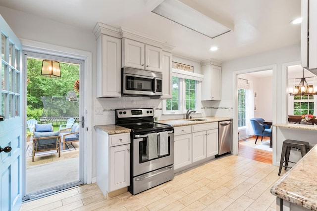 kitchen featuring appliances with stainless steel finishes, a sink, light wood-style flooring, decorative backsplash, and light stone counters