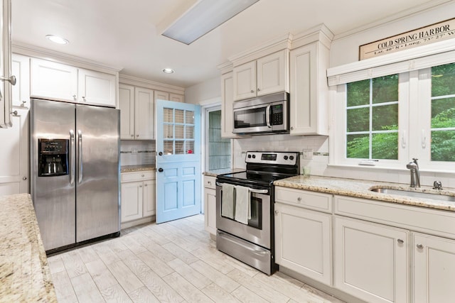 kitchen featuring appliances with stainless steel finishes, a sink, backsplash, light wood-style floors, and light stone countertops