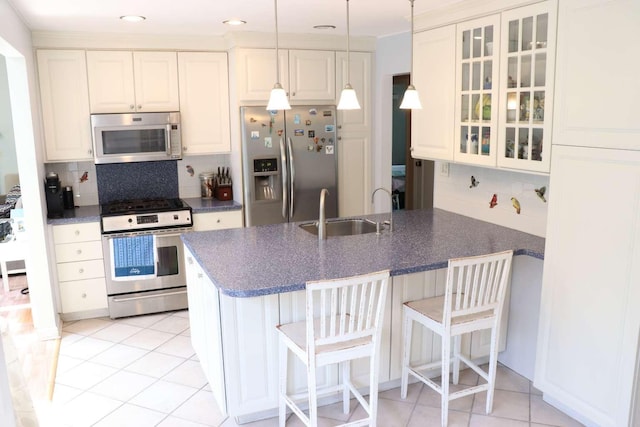 kitchen featuring appliances with stainless steel finishes, a sink, a peninsula, backsplash, and glass insert cabinets