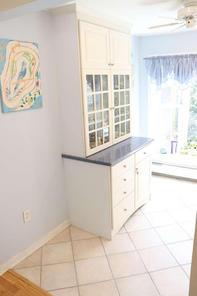 kitchen with ceiling fan, a baseboard radiator, light tile patterned floors, and white cabinetry