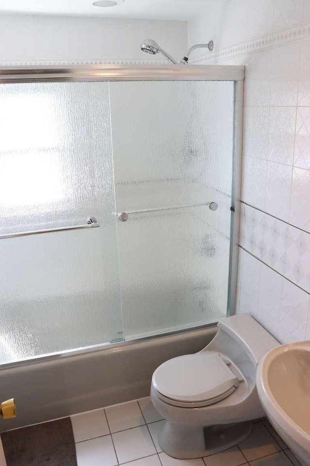 full bathroom featuring bath / shower combo with glass door, tile patterned floors, toilet, tile walls, and a sink