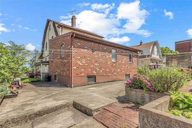 view of home's exterior featuring brick siding, a patio, and a chimney