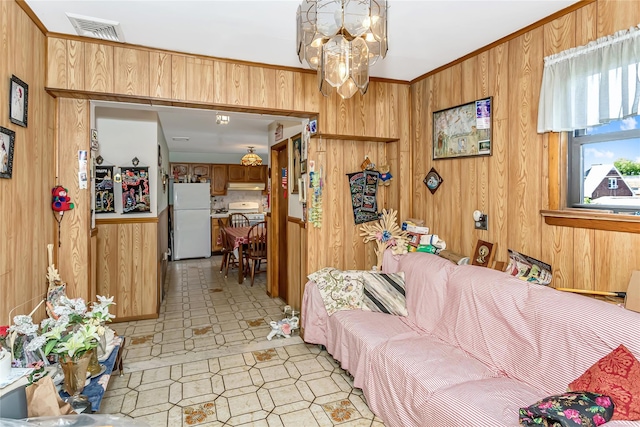 living area with wooden walls, a chandelier, light flooring, and ornamental molding