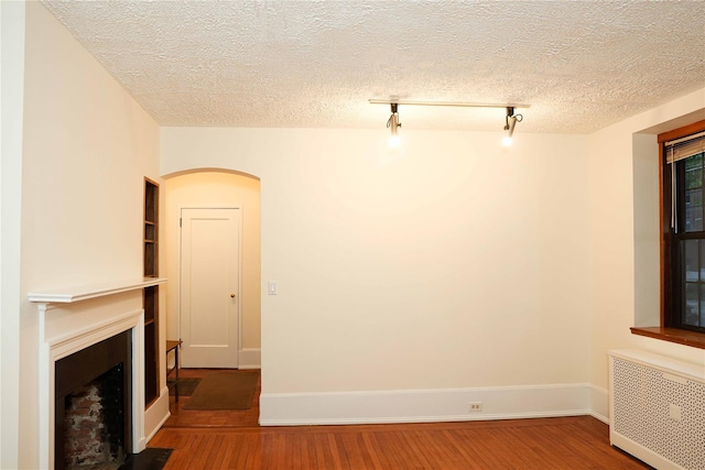 808 Bronx River Rd Unit 1A, Yonkers, NY 10708 - unfurnished living room featuring radiator heating unit, a fireplace with flush hearth, wood finished floors, arched walkways, and a textured ceiling