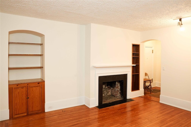 808 Bronx River Rd Unit 1A, Yonkers, NY 10708 - unfurnished living room with arched walkways, wood finished floors, a fireplace with flush hearth, and a textured ceiling
