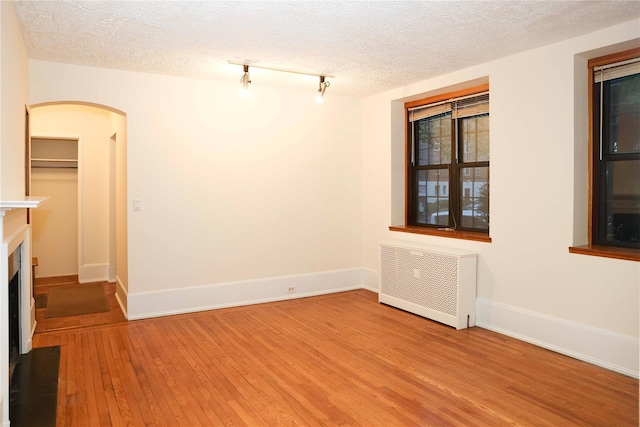 808 Bronx River Rd Unit 1A, Yonkers, NY 10708 - spare room with radiator, light wood-style flooring, arched walkways, baseboards, and a textured ceiling