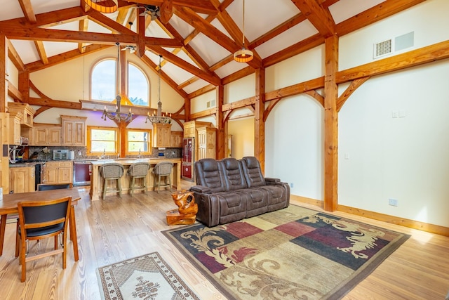 living area with a high ceiling, light wood-style floors, baseboards, beamed ceiling, and a chandelier