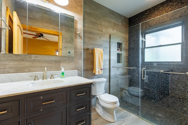 full bath featuring toilet, ceiling fan, a shower stall, vanity, and tile walls