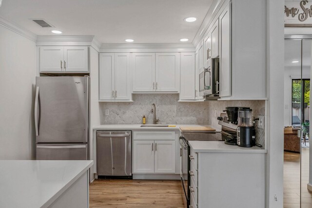 kitchen with a sink, appliances with stainless steel finishes, light countertops, white cabinetry, and recessed lighting