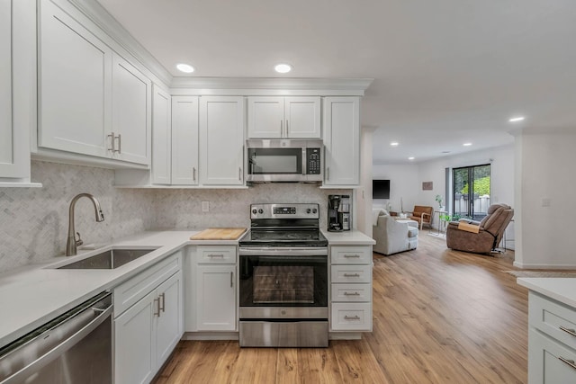 kitchen with appliances with stainless steel finishes, a sink, light countertops, open floor plan, and recessed lighting