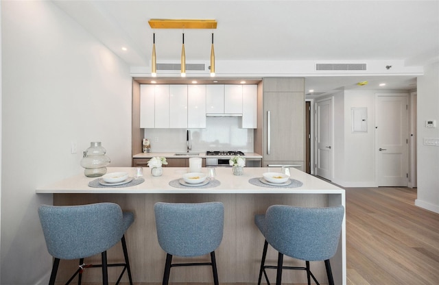 kitchen featuring a breakfast bar area, light countertops, a peninsula, white cabinets, and recessed lighting