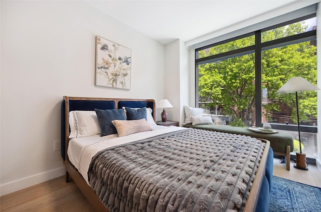 bedroom with baseboards, wood finished floors, and a wall of windows