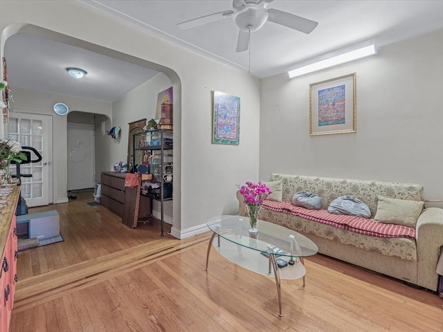 living room featuring ceiling fan, wood finished floors, arched walkways, and baseboards
