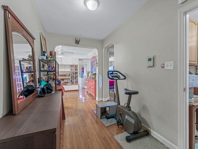 workout area with arched walkways, light wood-style flooring, baseboards, and ceiling fan