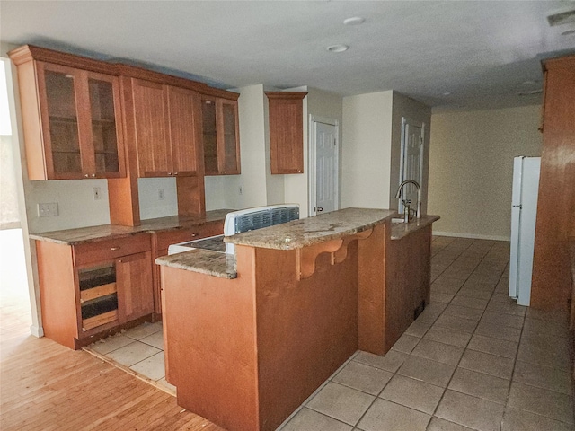 144 Union Ave, Patchogue, NY 11772 - kitchen featuring freestanding refrigerator, an island with sink, brown cabinetry, and glass insert cabinets