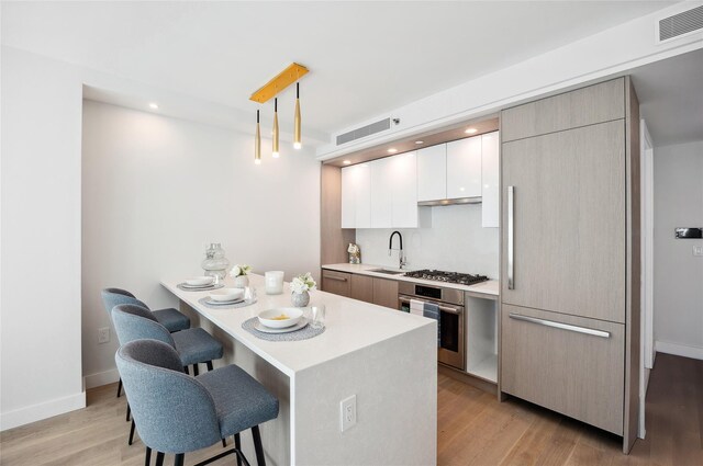kitchen with appliances with stainless steel finishes, a breakfast bar area, modern cabinets, light wood finished floors, and light countertops