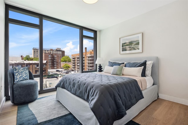 bedroom with a view of city, baseboards, wood finished floors, access to exterior, and floor to ceiling windows