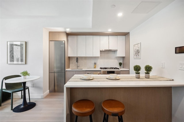 kitchen featuring stainless steel refrigerator, a kitchen breakfast bar, a sink, light wood-style flooring, and white cabinets