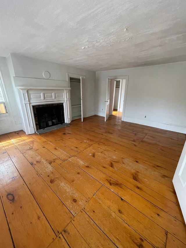 unfurnished living room featuring light wood-style floors, a textured ceiling, a fireplace, and baseboards