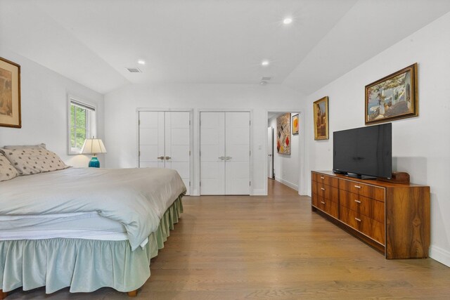 bedroom featuring wood finished floors, two closets, lofted ceiling, recessed lighting, and baseboards