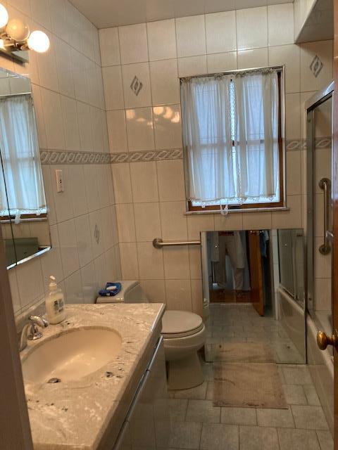 16615 67th Ave, Fresh Meadows, NY 11365 - bathroom featuring tile walls, vanity, toilet, bath / shower combo with glass door, and tile patterned flooring