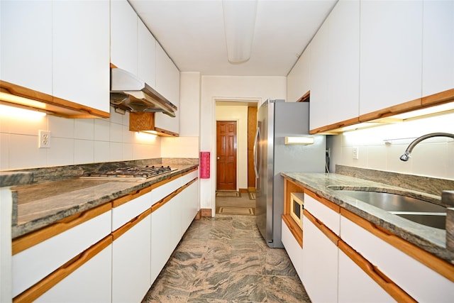 kitchen featuring appliances with stainless steel finishes, under cabinet range hood, white cabinets, a sink, and decorative backsplash