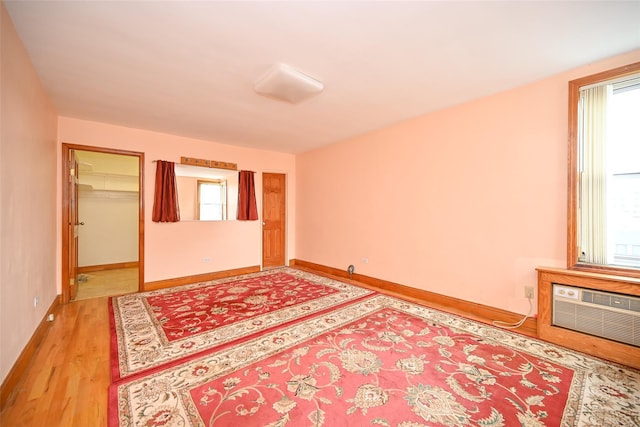 unfurnished bedroom with multiple windows, a wall mounted air conditioner, light wood-style flooring, and baseboards