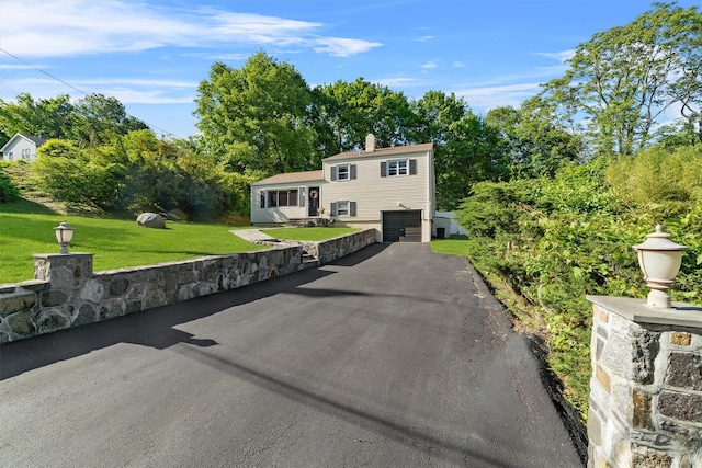 10 Ridge Rd, Cortlandt Manor, NY 10567 - tri-level home with asphalt driveway, an attached garage, a front lawn, a chimney, and view of wooded area