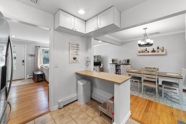 10 Ridge Rd, Cortlandt Manor, NY 10567 - kitchen with a baseboard heating unit, crown molding, a chandelier, white cabinets, and stainless steel refrigerator with ice dispenser
