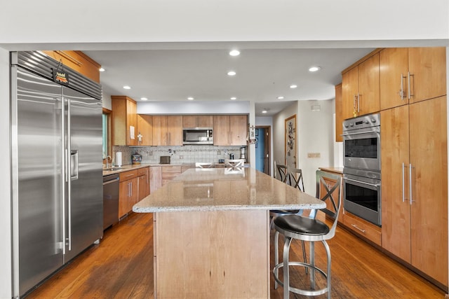 1260 Albany Post Rd, Croton-On-Hudson, NY 10520 - kitchen featuring stainless steel appliances, dark wood-type flooring, a kitchen island, light stone countertops, and a kitchen bar