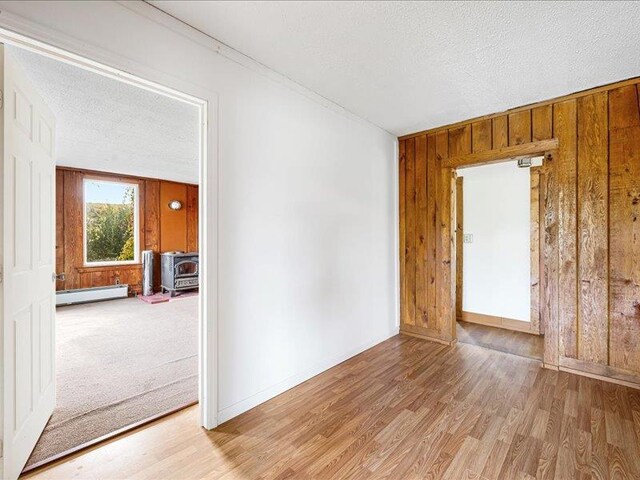 58 Hathorn Blvd, Port Jervis, NY 12771 - empty room featuring a baseboard radiator, a wood stove, wood walls, light wood-style flooring, and a textured ceiling