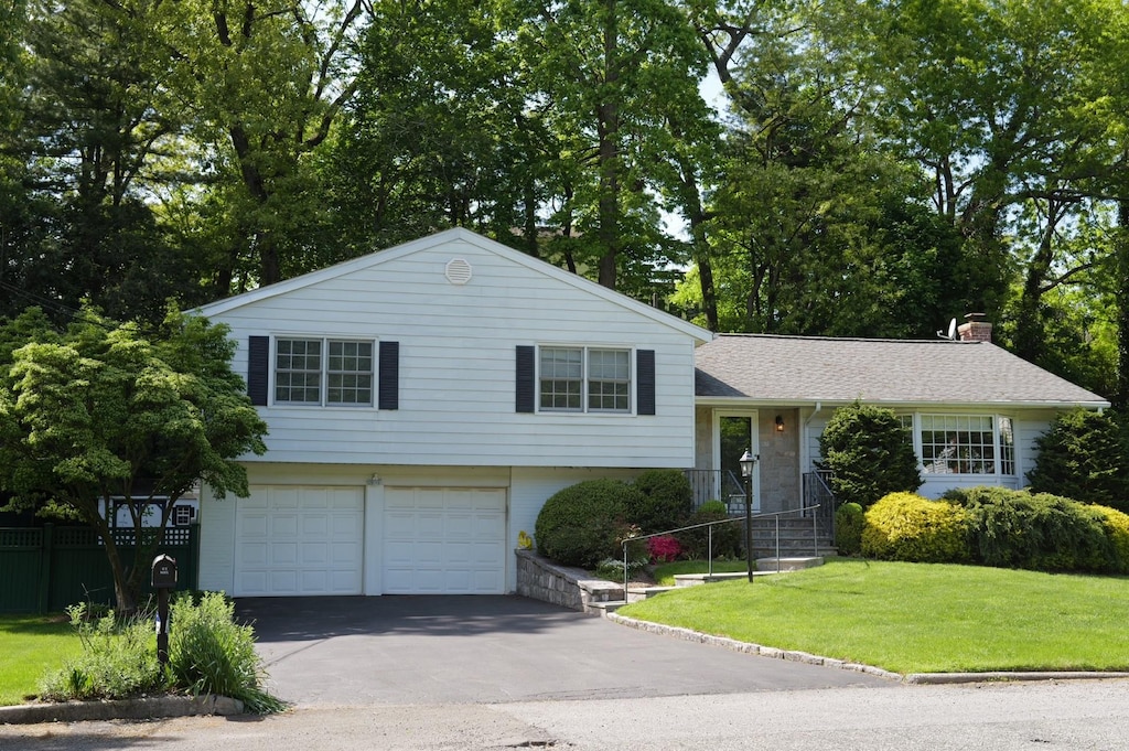 split level home with an attached garage, driveway, a chimney, and a shingled roof