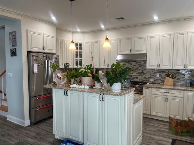kitchen with freestanding refrigerator, under cabinet range hood, dark wood-type flooring, tasteful backsplash, and white cabinets