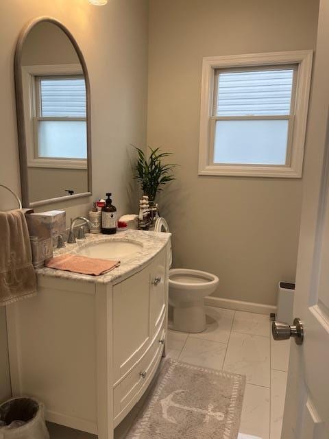 bathroom with vanity, healthy amount of natural light, toilet, and marble finish floors
