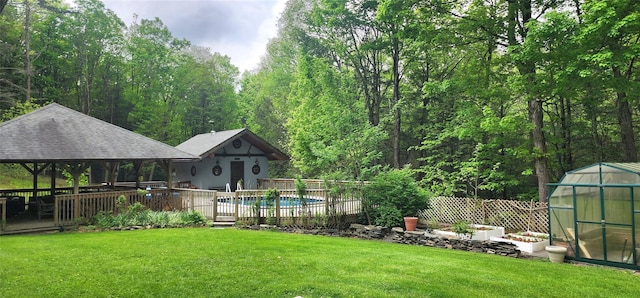 view of yard with a greenhouse, an outdoor structure, a gazebo, a view of trees, and a wooden deck