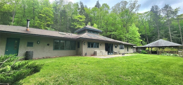 back of property featuring a gazebo, stucco siding, a lawn, a patio area, and a forest view