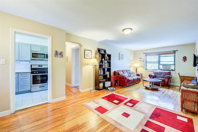 living area featuring light wood-type flooring, arched walkways, and baseboards