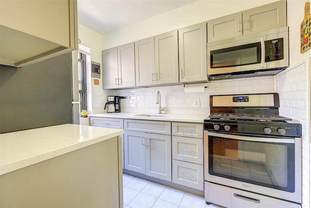 kitchen with appliances with stainless steel finishes, a sink, gray cabinets, decorative backsplash, and light tile patterned floors