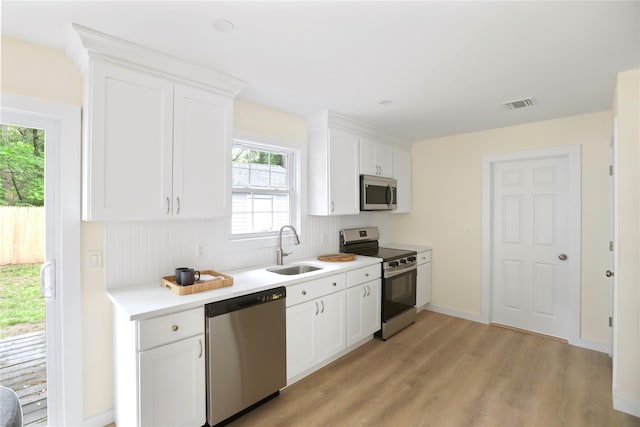 kitchen with stainless steel appliances, a sink, light countertops, light wood-type flooring, and white cabinets