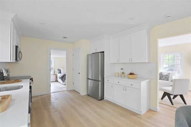 kitchen featuring appliances with stainless steel finishes, light wood-style flooring, white cabinetry, and light countertops
