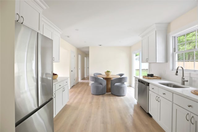 kitchen with appliances with stainless steel finishes, a sink, light countertops, light wood-type flooring, and white cabinets