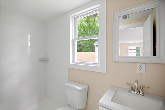 bathroom with toilet, a tile shower, and vanity
