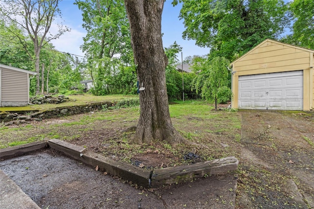 view of yard featuring a garage, driveway, and an outbuilding