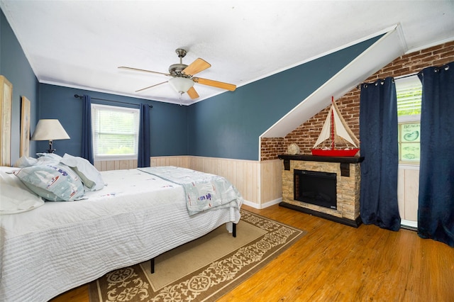 136 Foggintown Rd, Brewster, NY 10509 - bedroom with wood finished floors, multiple windows, a wainscoted wall, ceiling fan, and a stone fireplace