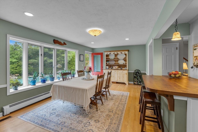 dining area with a baseboard heating unit, light wood-style floors, a textured ceiling, recessed lighting, and baseboards