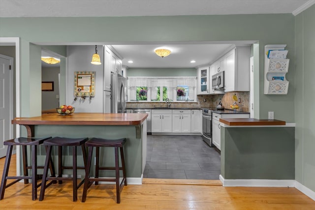 kitchen with appliances with stainless steel finishes, wood counters, a kitchen bar, a sink, and white cabinets
