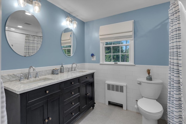full bathroom featuring radiator, a wainscoted wall, tile walls, double vanity, and toilet