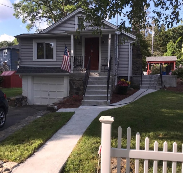 bungalow-style house featuring an attached garage, covered porch, a front lawn, and asphalt driveway
